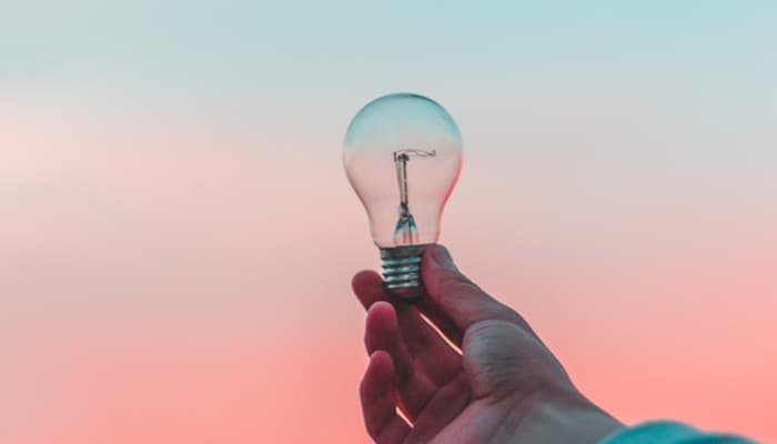 Person holding a lightbulb with light blue and pink sky in the background